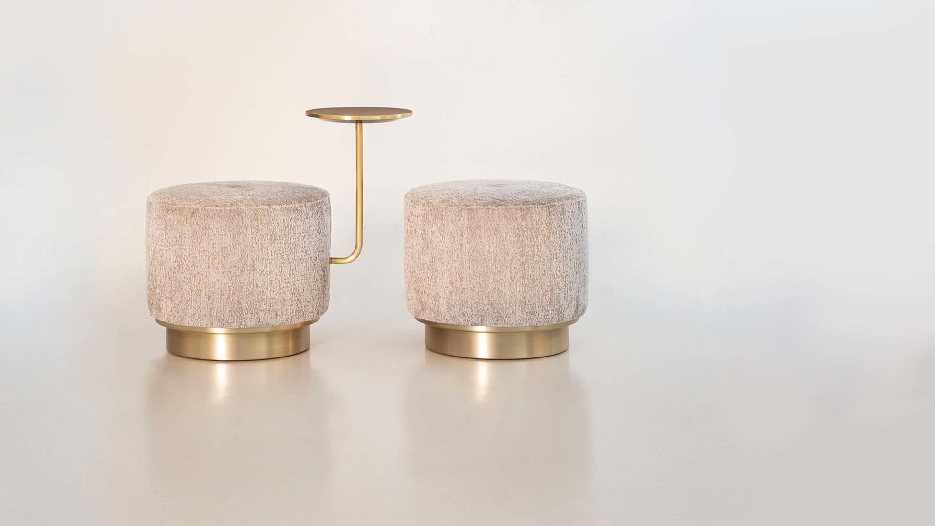 Harry pouf | Rugiano. Versatile upholstered poufs with elegant satin gold details, available in classic, armrest, and integrated side table designs.